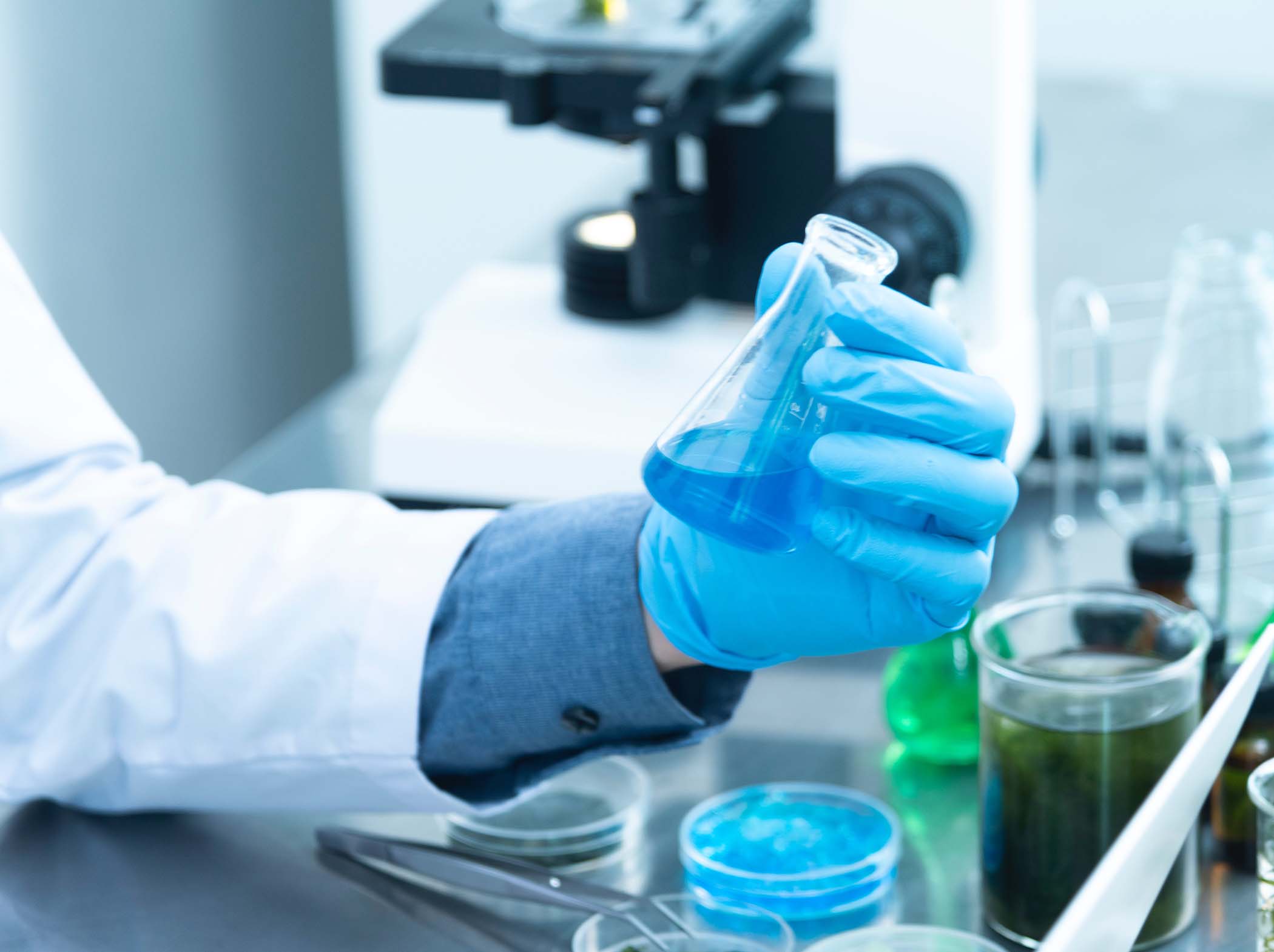 gloved hand holds a flask with liquid in a laboratory environment